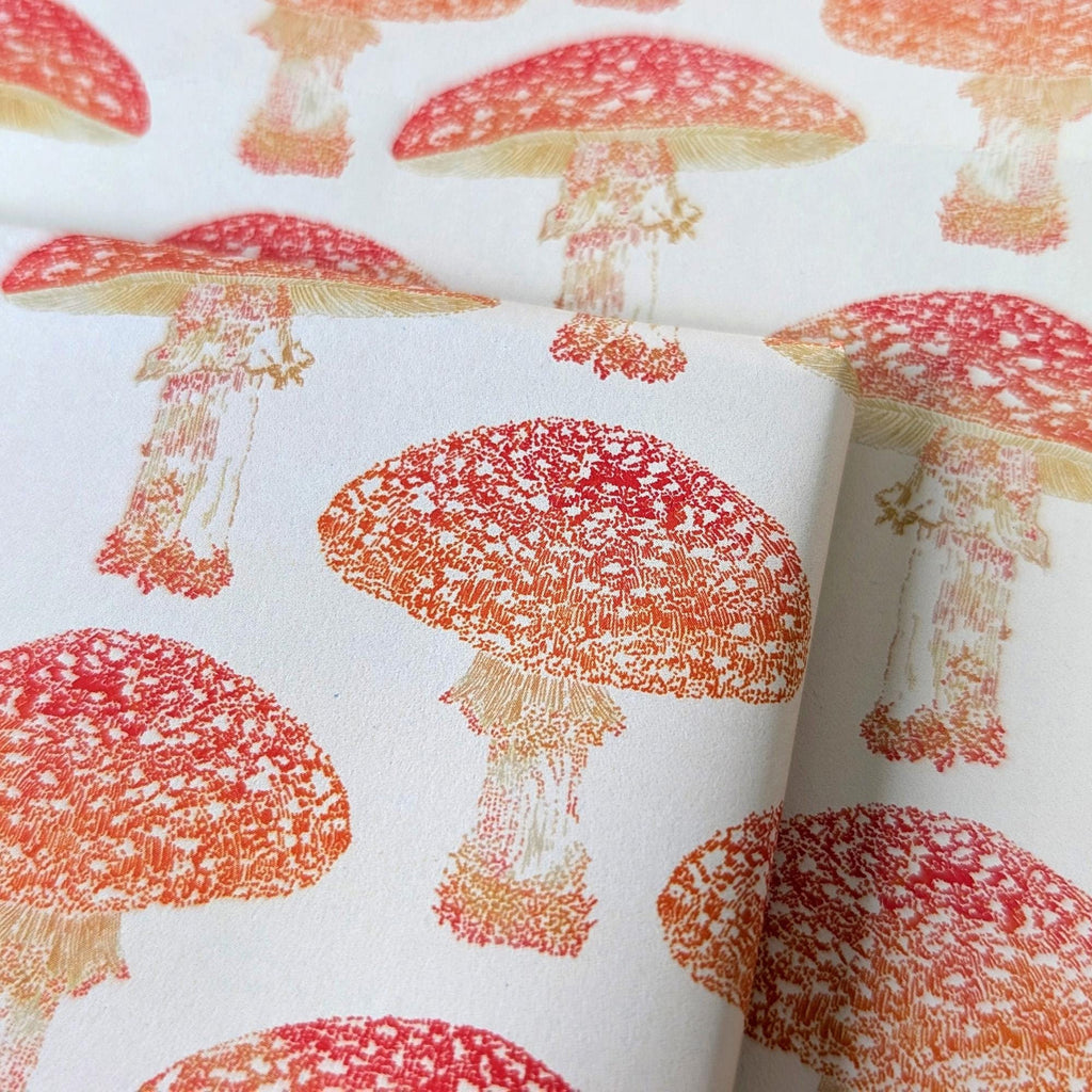 A close-up of a white gift wrap with a repeating pattern of red and orange toadstools, showing the texture and print.