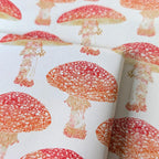 A close-up of a white gift wrap with a repeating pattern of red and orange toadstools, showing the texture and print.