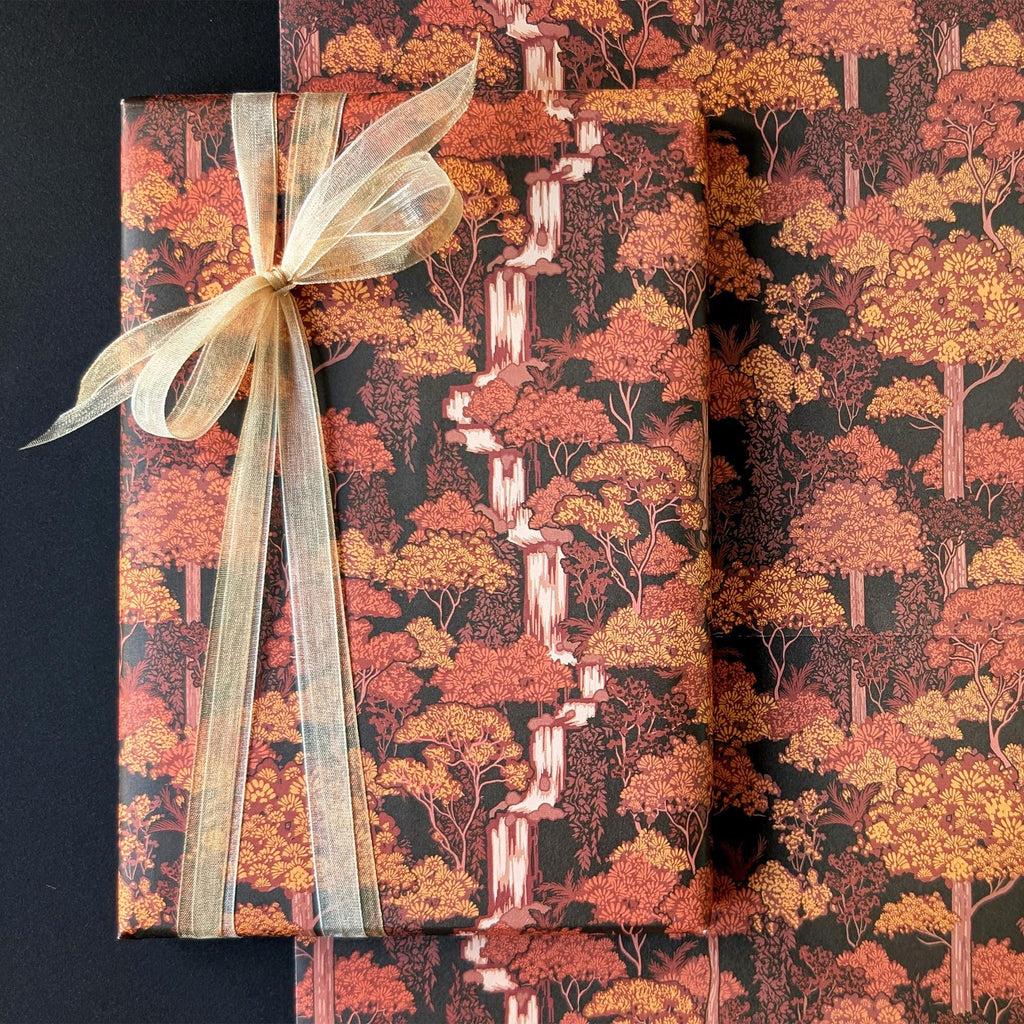 Autumn forest patterned wrapping paper shown wrapped around gift boxes, featuring orange, red, and yellow trees on a dark background with a sheer beige ribbon bow.