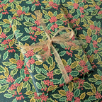 A gift-wrapped package covered in dark green holiday paper with a holly and red berries pattern, tied with a sheer beige ribbon.