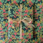 A gift wrapped in festive holly-patterned wrapping paper tied with a sheer beige ribbon, shown from a top-down view.